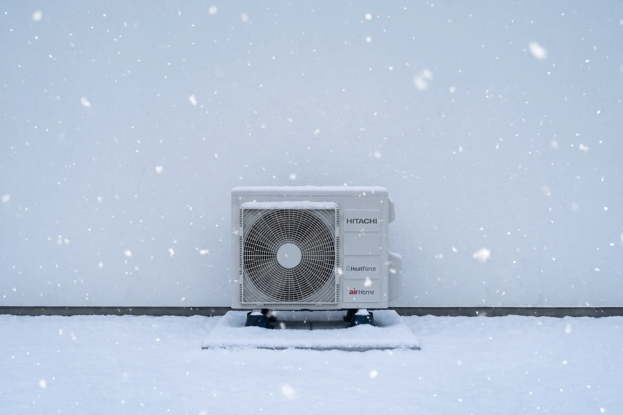 Hitachi airHome outdoor heat pump unit with HeatForce badging, running in falling snow